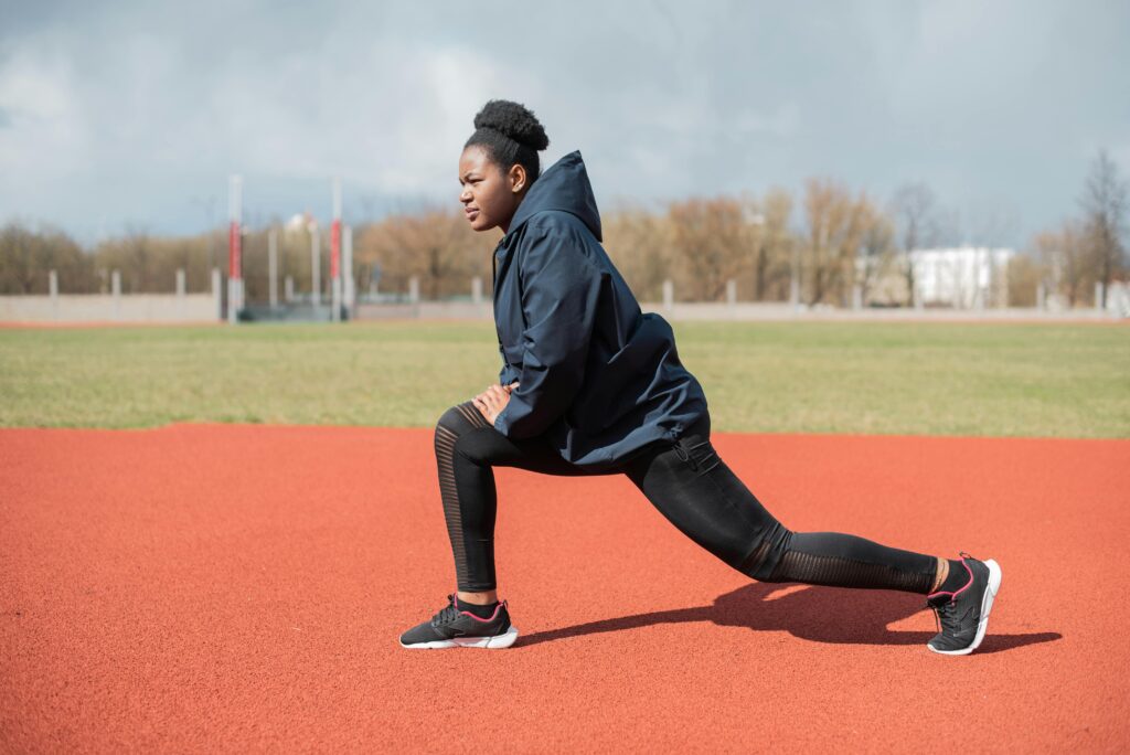 Woman in Black Hoodie Doing Lunges on Track and Field